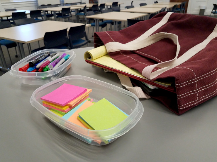 Post-it notes and markers spilling out of a bag at the front of a classroom.